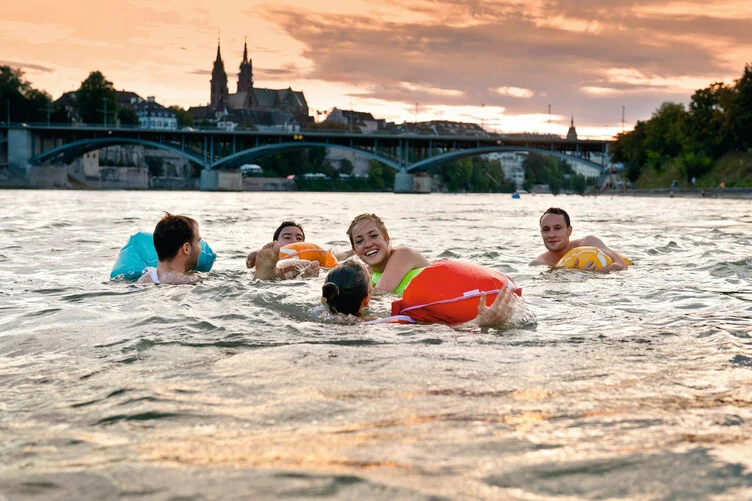 Gruppe von Menschen schwimmt im Rhein bei Basel mit Sicht auf die Mittlere Brücke